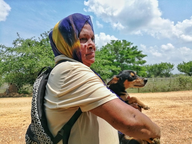 Foto vista lateral de uma mulher com um cão olhando para longe contra as árvores e o céu