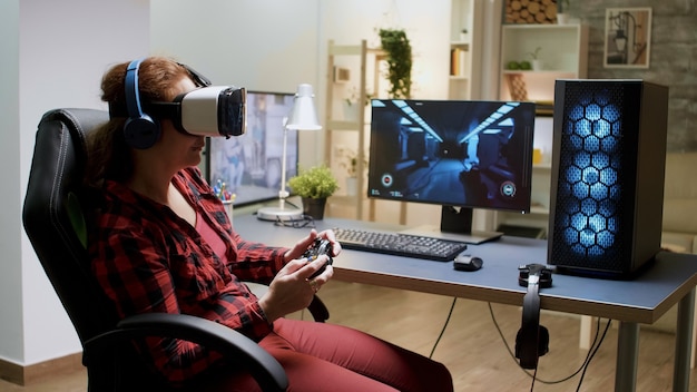 Vista lateral de uma mulher de cabelo vermelho usando óculos de proteção vr enquanto jogava videogame com controlador sem fio.