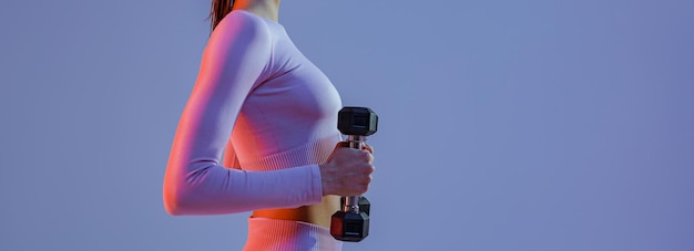 Vista lateral de uma mulher de fitness fazendo exercícios com halteres no fundo do estúdio