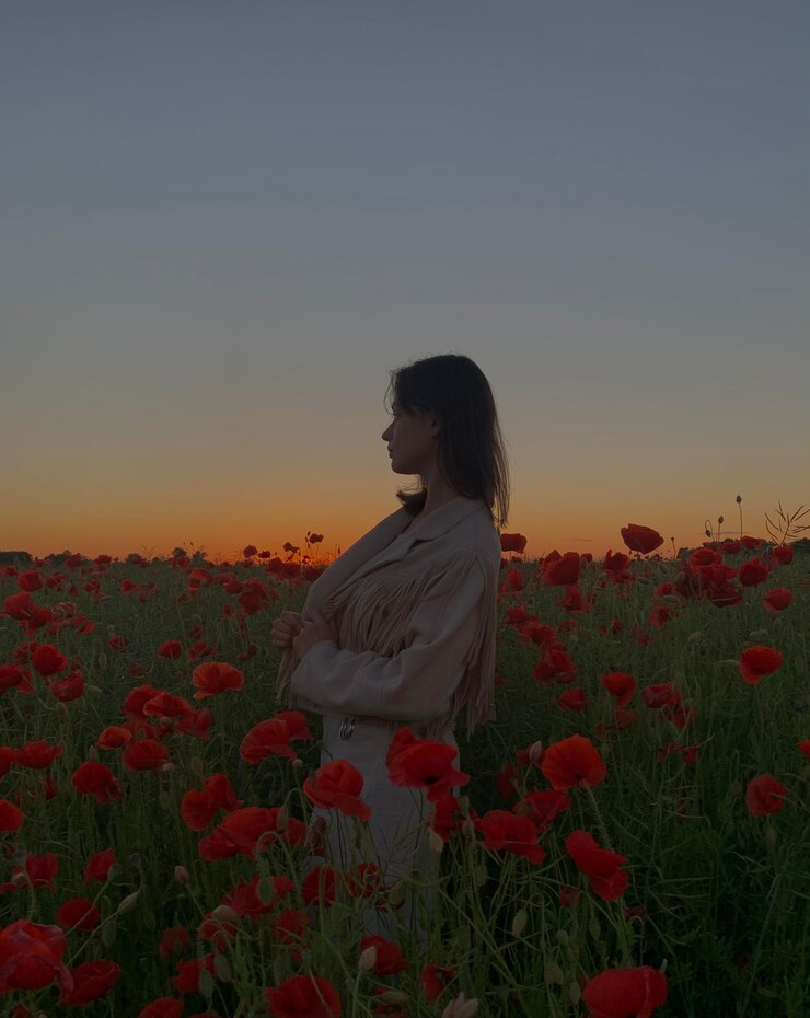 Foto vista lateral de uma mulher de pé em um campo de papoula vermelha contra o céu durante o pôr-do-sol