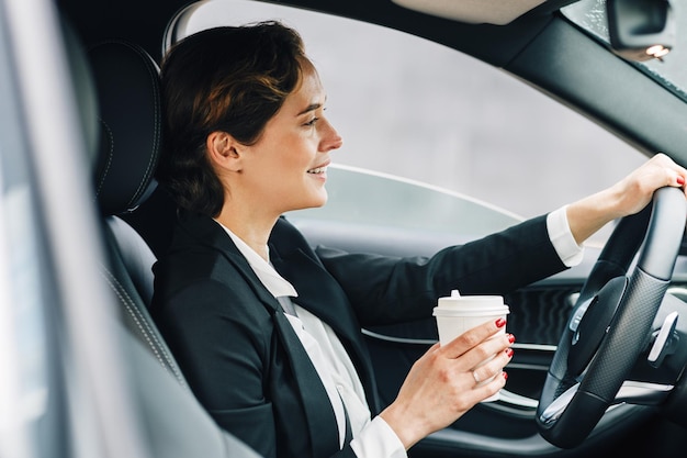 Vista lateral de uma mulher dirigindo um carro enquanto bebe café