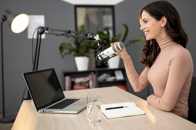 Vista lateral de uma mulher em um estúdio de rádio com laptop e microfone