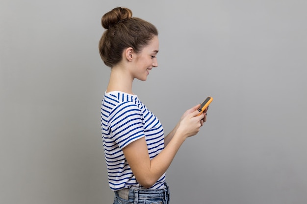 Foto vista lateral de uma mulher feliz lendo uma mensagem no smartphone sorrindo usando um dispositivo móvel navegando na web