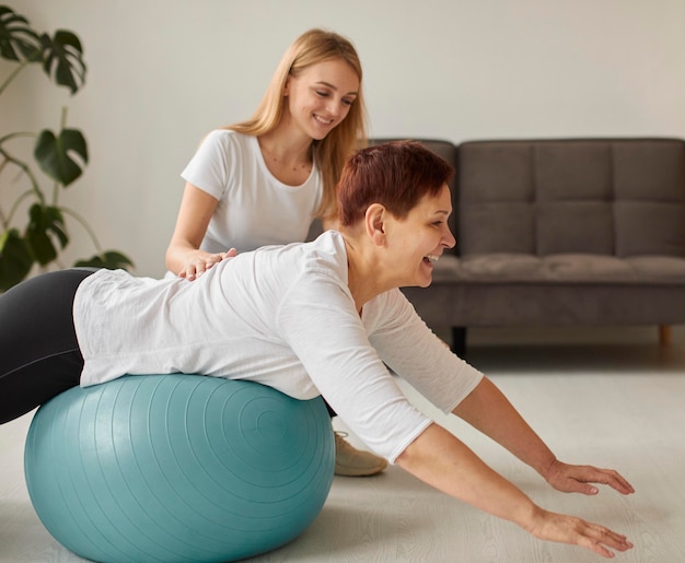 Vista lateral de uma mulher idosa sorridente em recuperação cobiçosa fazendo exercícios com a bola