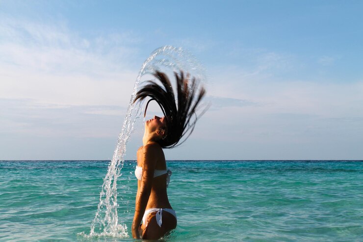 Foto vista lateral de uma mulher jogando o cabelo no mar contra o céu