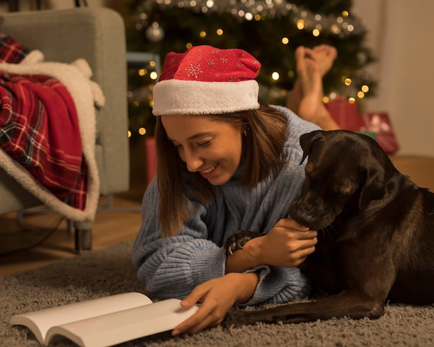 Vista lateral de uma mulher lendo um livro de Natal com seu cachorro