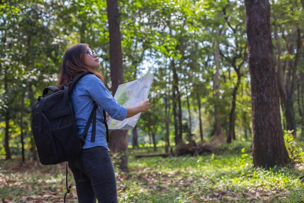 Foto vista lateral de uma mulher segurando um mapa enquanto está de pé na floresta