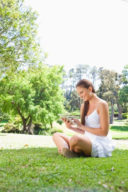 Vista lateral de uma mulher sorridente no gramado com um tablet computador