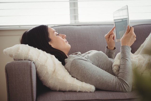 Vista lateral de uma mulher usando o tablet enquanto estava deitada no sofá