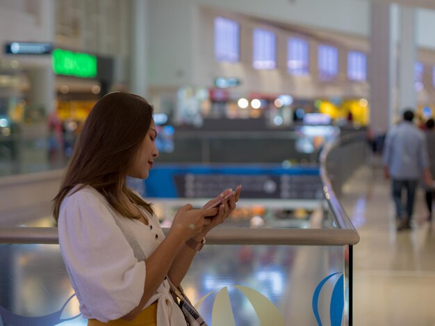 Foto vista lateral de uma mulher usando um telefone inteligente enquanto está de pé em um shopping