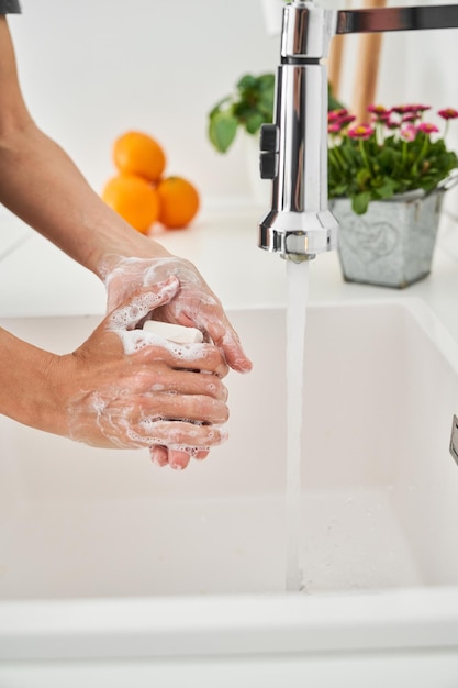 Vista lateral de uma pessoa anônima esfregando as mãos enquanto espalha sabão nas mãos para lavar na pia do banheiro