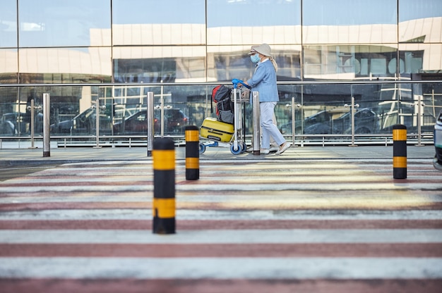 Foto vista lateral de uma turista idosa caucasiana e seu marido empurrando o carrinho de bagagem