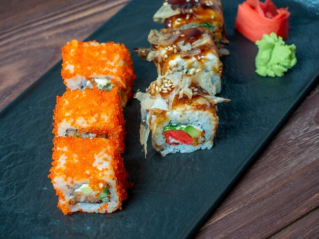 Vista lateral de deliciosos rollos jugosos decorados con caviar. Cocina japonesa, plato negro, cerrar