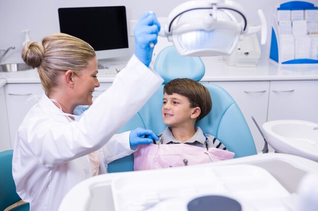 Vista lateral del dentista ajustando la luz eléctrica mientras el niño sentado en una silla