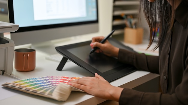 Vista lateral de la diseñadora que trabaja con tableta de dibujo y muestra de color en el escritorio de la computadora
