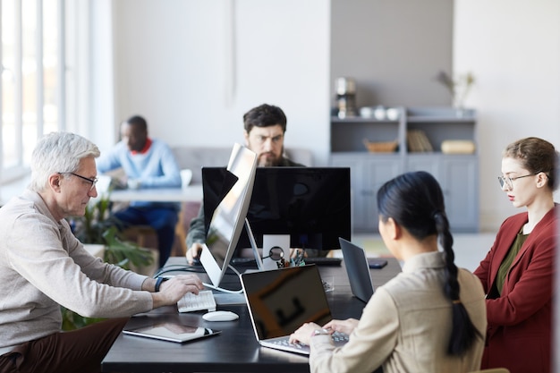 Vista lateral en diverso grupo de gente de negocios que trabaja con computadoras en la oficina moderna, se centran en el hombre mayor en el estudio de TI