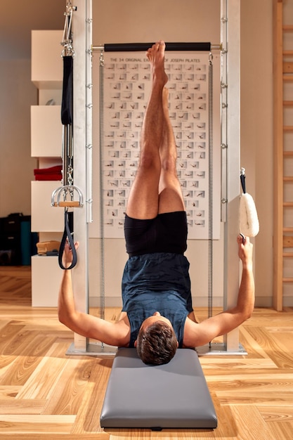 Vista lateral do atleta masculino descalço deitado no reformador de pilates e realizando exercícios abdominais durante o treino de fitness Conceito de homem de Pilates