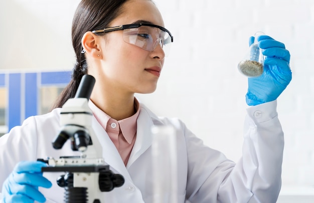 Vista lateral do cientista feminina com microscópio e luvas cirúrgicas