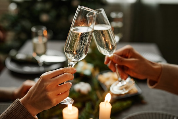 Vista lateral do close up de um jovem casal tilintando taças de champanhe enquanto desfruta do jantar de Natal juntos.