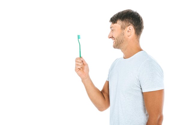 Foto vista lateral do homem alegre olhando para a escova de dentes enquanto sorri isolado no branco