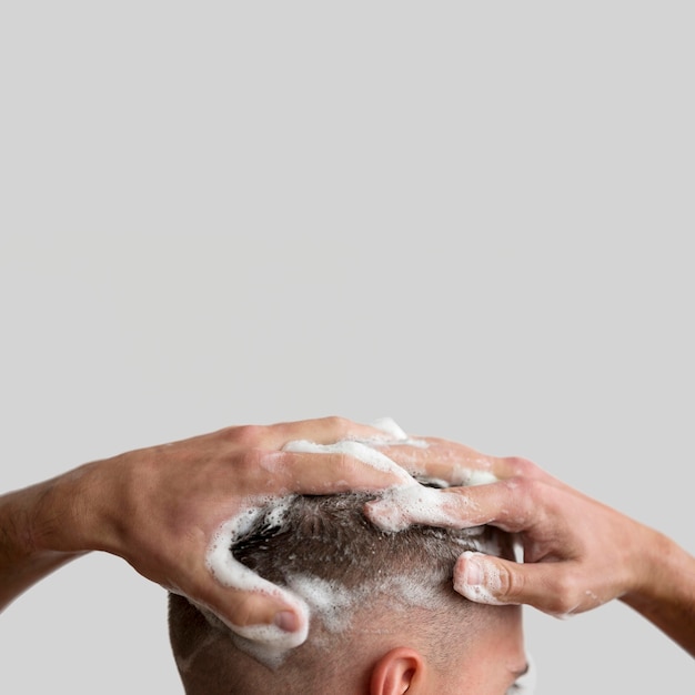Vista lateral do homem lavando o cabelo com shampoo