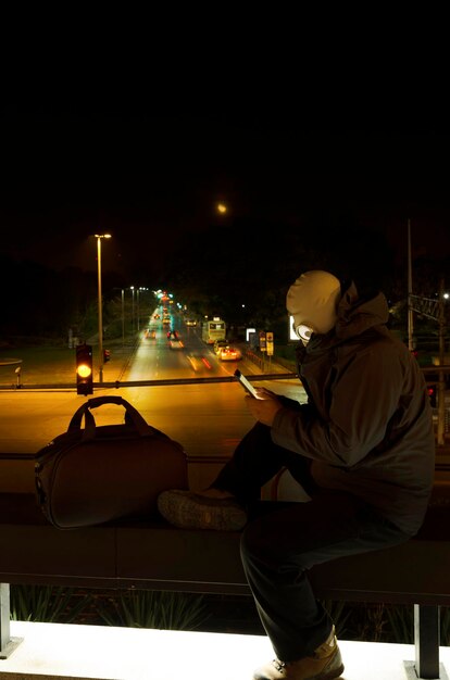 Vista lateral do homem sentado na cidade iluminada contra o céu à noite