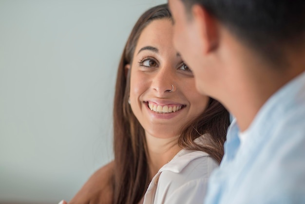 Vista lateral do retrato de mulher feliz sorrindo e olhando o namorado jovem casal apaixonado e relacionamento amizade entre homem e mulher fundo branco pessoas de lazer em casa interior