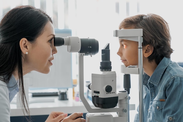 Vista lateral de una doctora oftalmóloga revisando la visión de un niño lindo en la clínica