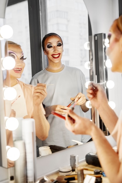 Foto vista lateral drag queens sonriendo en el espejo