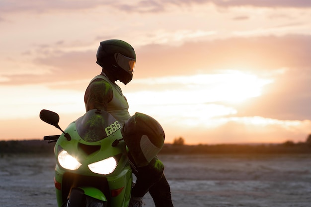 Vista lateral de un elegante motociclista masculino con casco parado cerca de una moto moderna