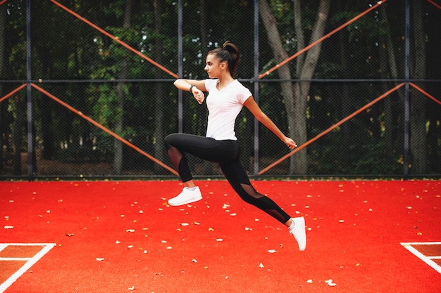 Vista lateral de una encantadora joven saltando en un parque deportivo por la mañana.