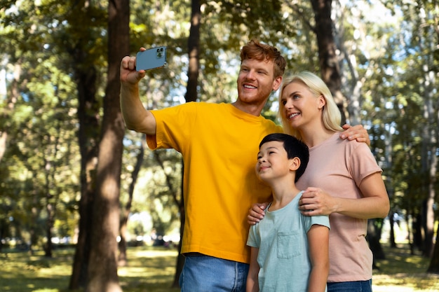 Vista lateral familia sonriente tomando selfie en la naturaleza