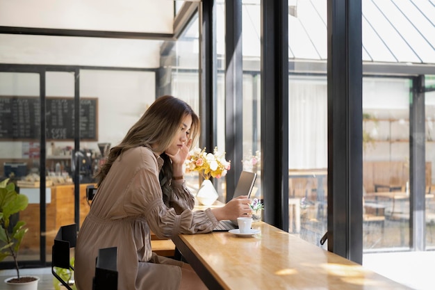 Foto vista lateral freelancer de mulher asiática usando laptop de computador enquanto está sentado no café brilhante