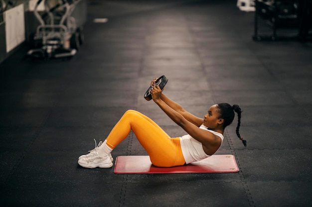 Vista lateral de una fuerte deportista negra haciendo abdominales con placa de peso en el gimnasio