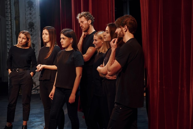 Foto vista lateral grupo de actores con ropa de color oscuro en el ensayo en el teatro