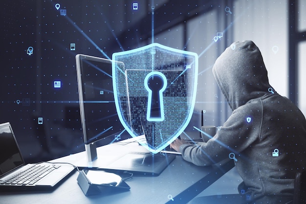Vista lateral de un hacker en el escritorio usando computadoras con escudo de seguridad web brillante creativo en el fondo borroso del interior de la oficina Concepto de información segura Doble exposición