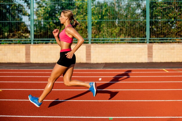 Vista lateral hermosa mujer joven ejercicio trotar y correr en la pista de atletismo en el estadio. Deporte, concepto de estilo de vida saludable.