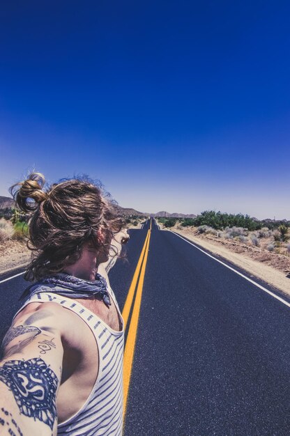 Foto vista lateral de un hombre apuntando a la carretera contra el cielo azul