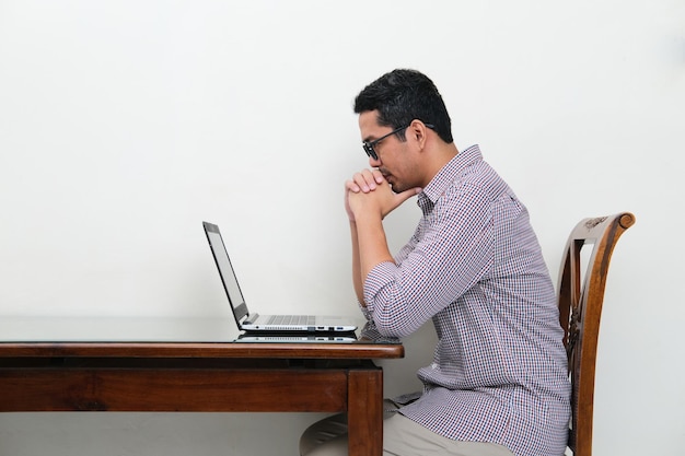 Foto vista lateral del hombre asiático mirando a su computadora portátil con una expresión de enfoque seria