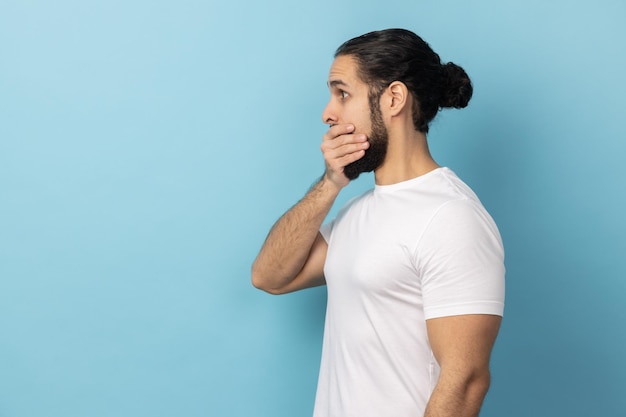 Vista lateral del hombre con barba con camiseta blanca que cubre la boca no quiere difundir rumores