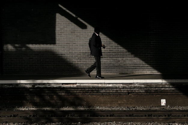 Vista lateral de un hombre caminando por la plataforma de la estación de tren