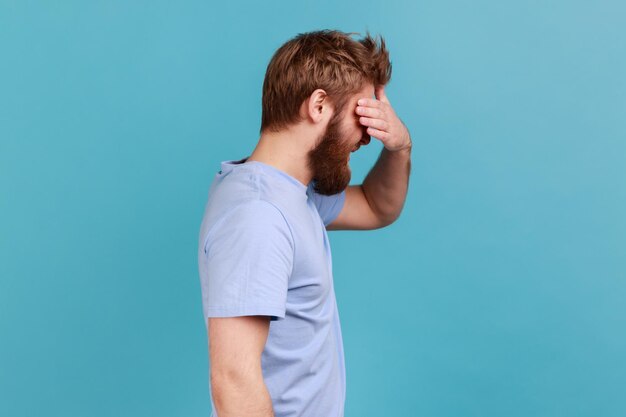 Vista lateral del hombre con camiseta azul cubriendo los ojos y girando con disgusto por algo vergonzoso