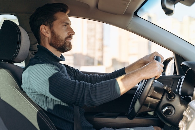 Vista lateral del hombre confiado serio que viaja en el automóvil y se siente confiado mientras mira la carretera durante la conducción. Foto de stock