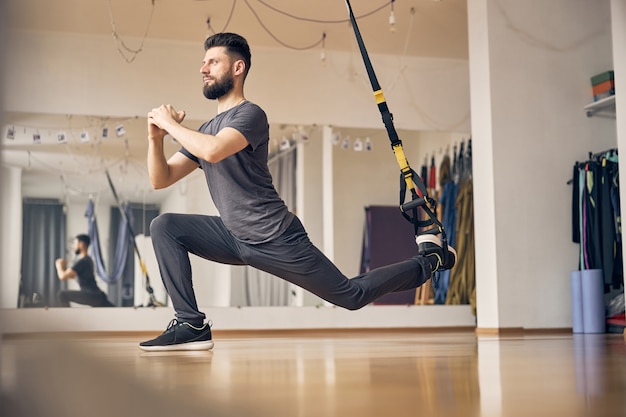 Vista lateral de un hombre deportivo trabajando en un entrenador de suspensión en un gimnasio