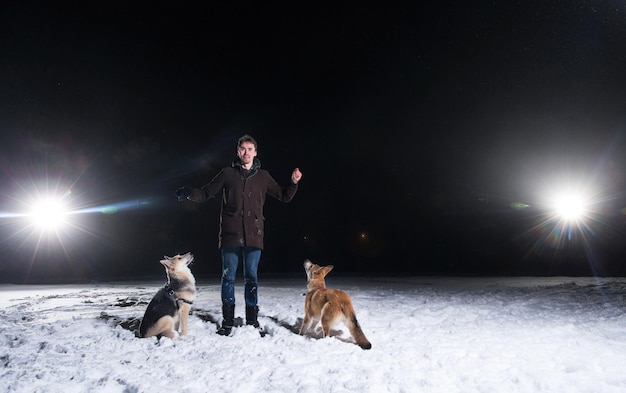 Vista lateral de un hombre con dos perros de raza mixta afuera por la noche en invierno