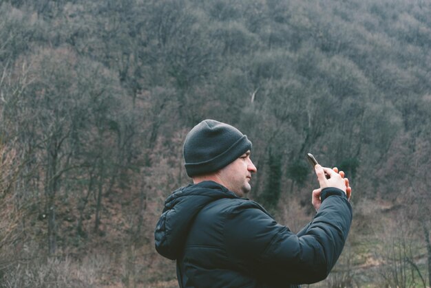 Foto vista lateral de un hombre fotografiando contra árboles desnudos en la montaña