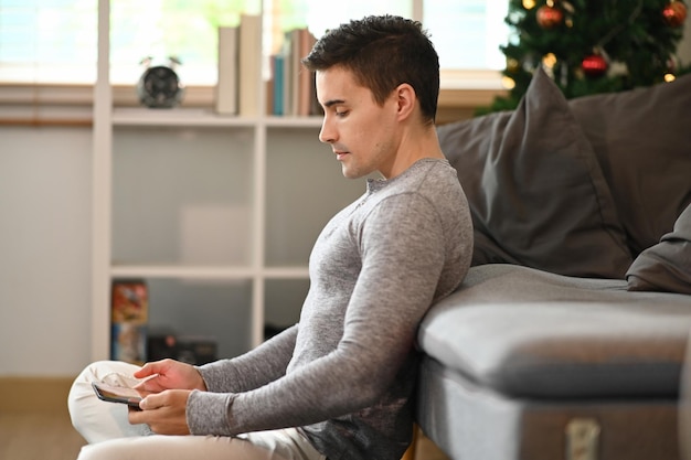 Vista lateral de un hombre guapo con ropa informal usando una tableta digital en casa