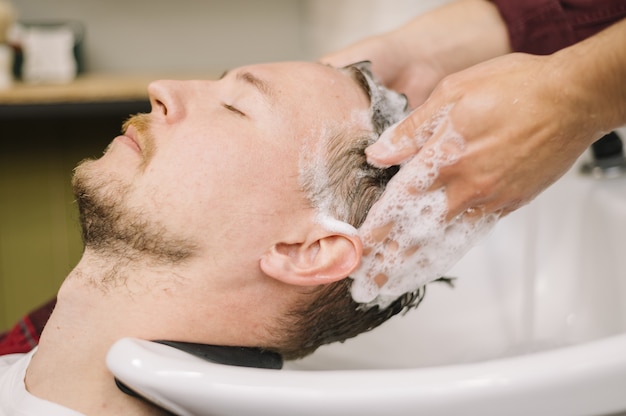Foto vista lateral del hombre lavarse el cabello en la peluquería