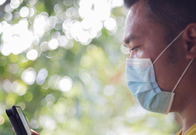 Foto vista lateral de un hombre con una máscara usando un teléfono inteligente