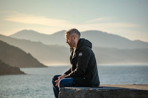 Foto vista lateral de un hombre mirando al mar contra el cielo durante la puesta de sol